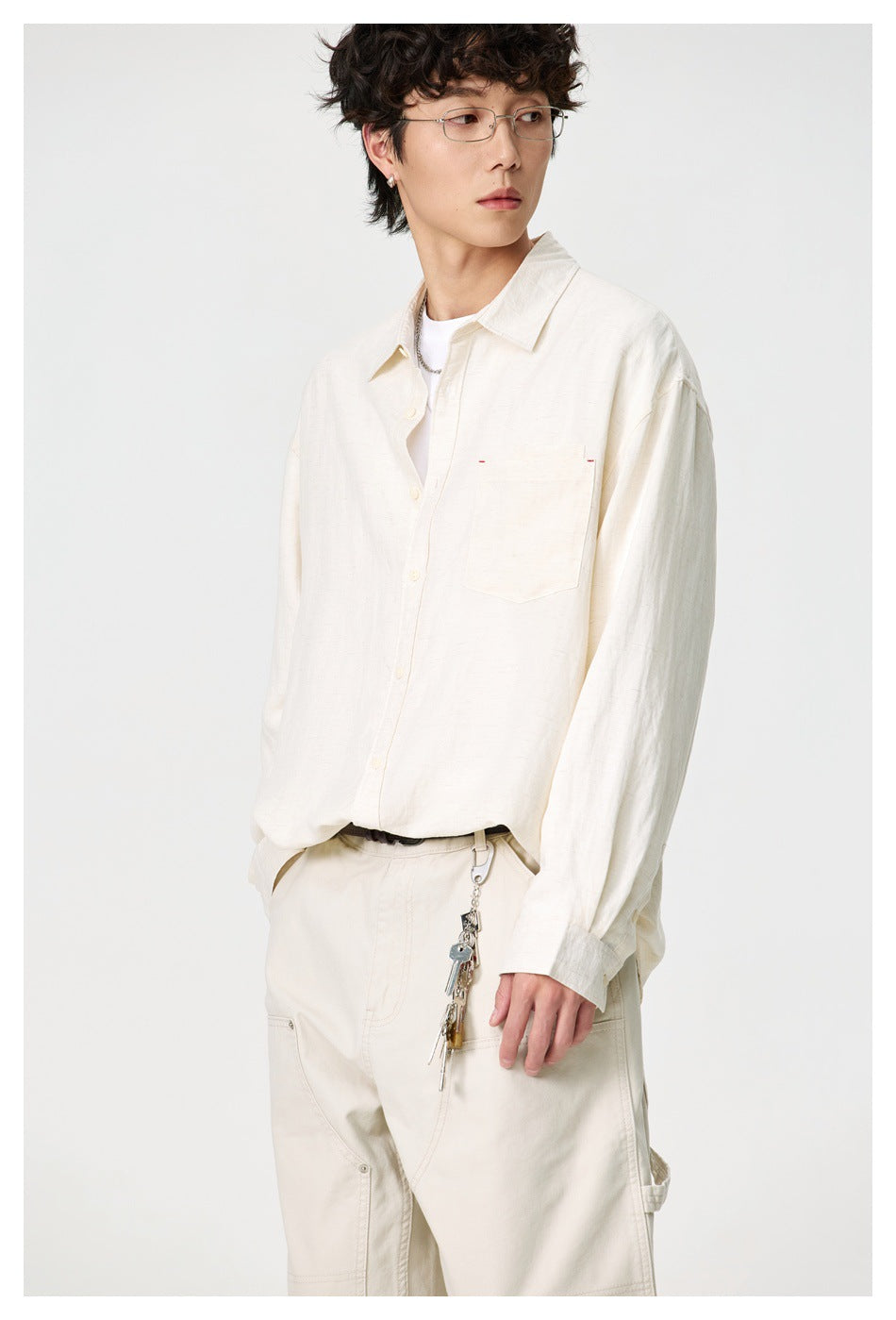 Model wearing an ivory button-up shirt and light utility trousers, shown from head to mid-thigh.