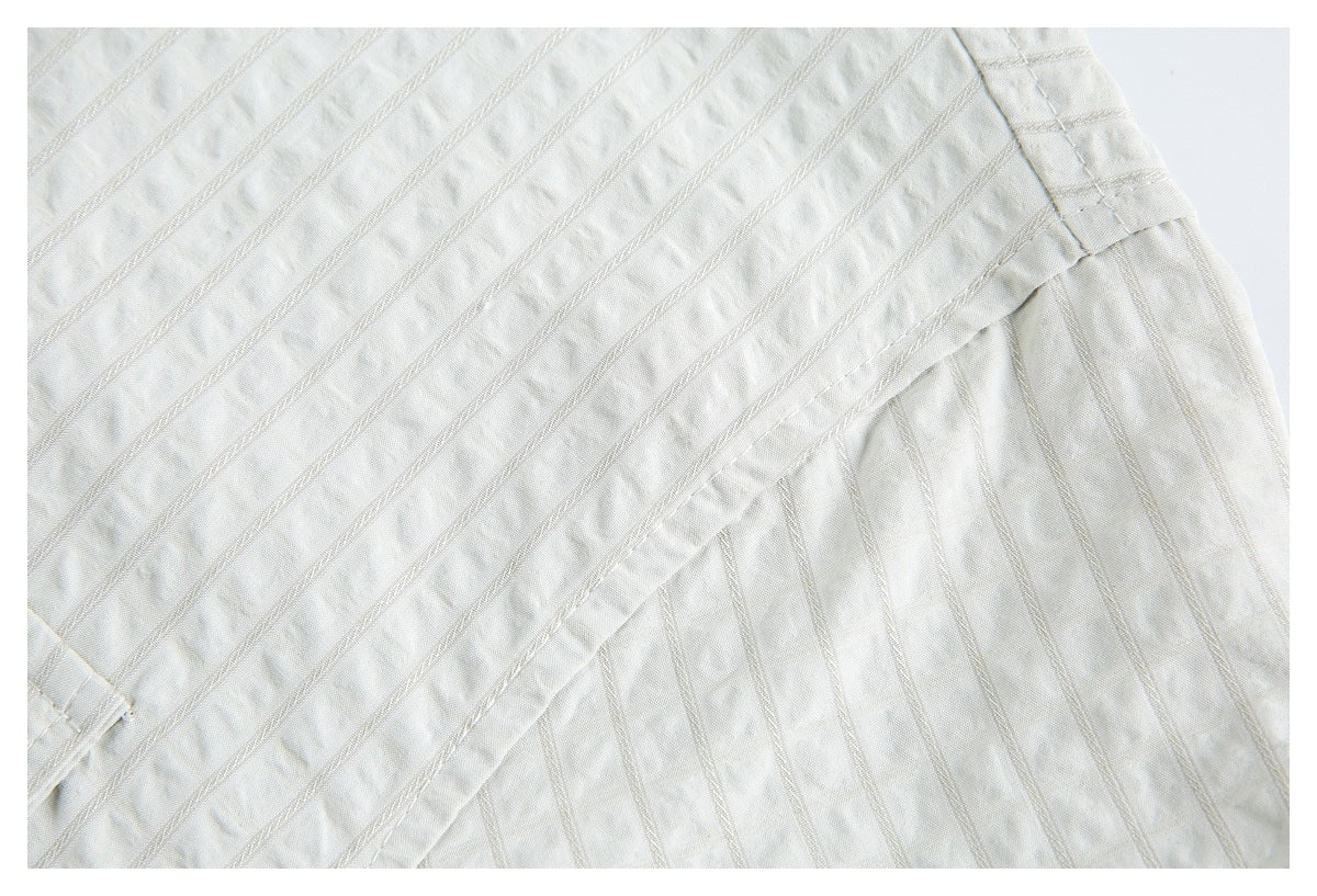 Close-up of ivory fabric with narrow diagonal stitched stripes and a gathered seam.