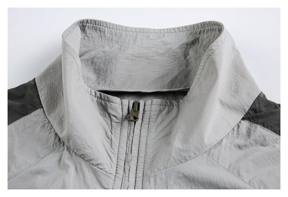 Close-up of a light gray jacket's tall collar, front zipper, and dark contrasting shoulder panels.