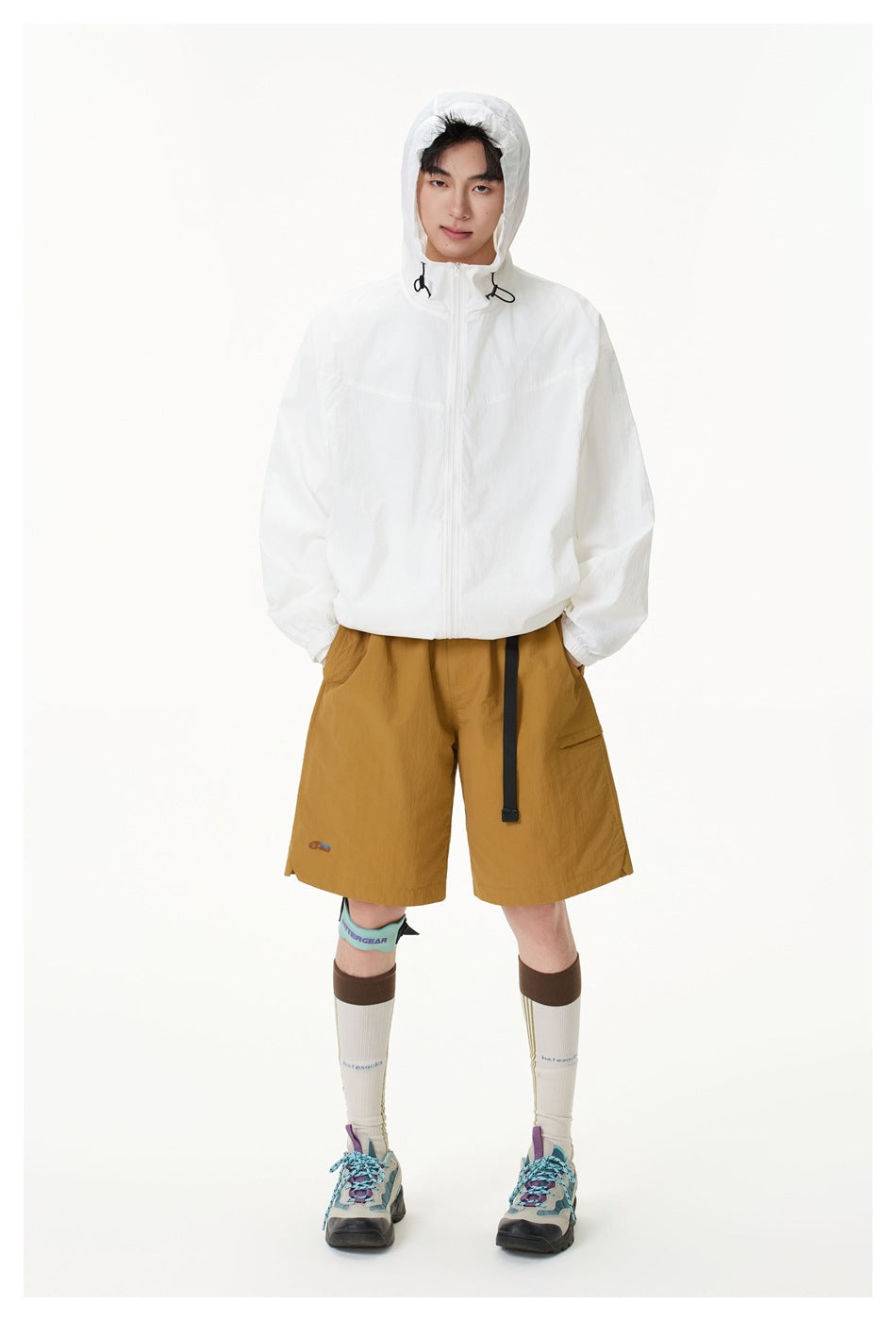 Front view of a model wearing a white hooded zip jacket with mustard shorts; the hood is up.