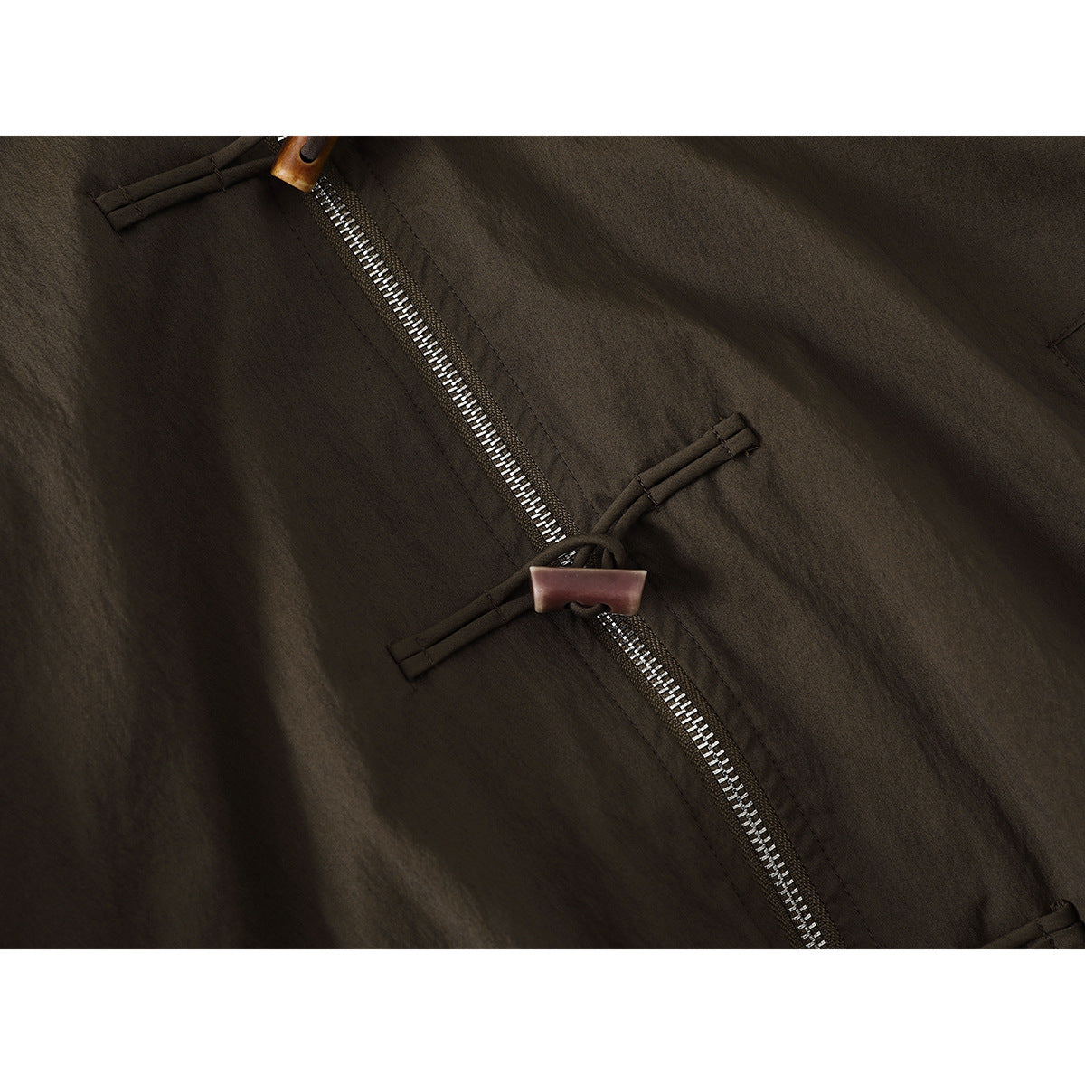 Close-up of the jacket’s metal front zipper and toggle closure against dark olive-brown fabric.