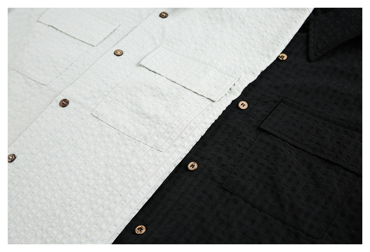 Close view of white and black button-up shirts with textured vertical stripes, chest pockets, and brown buttons.