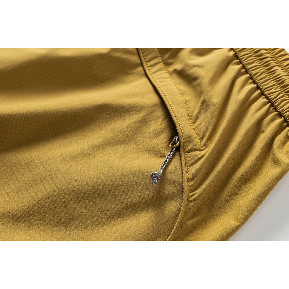 Close-up of a mustard-yellow trouser pocket with a cord pull and elastic waistband visible.