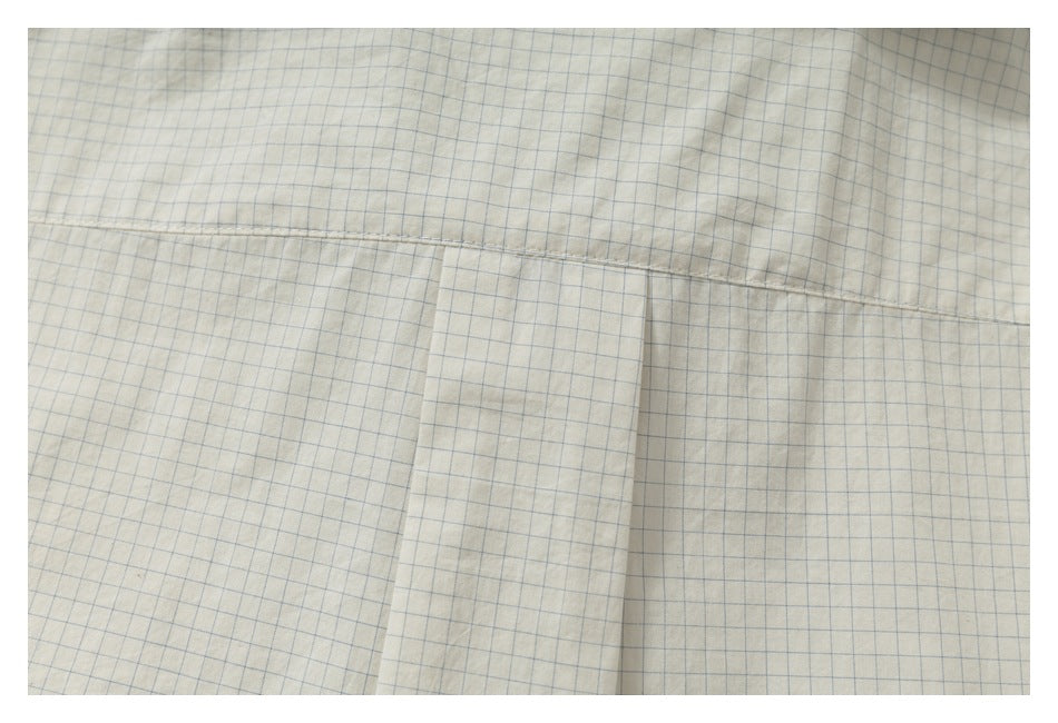 Close-up of a horizontal stitched seam and vertical fabric panel on a cream shirt with a fine blue grid.