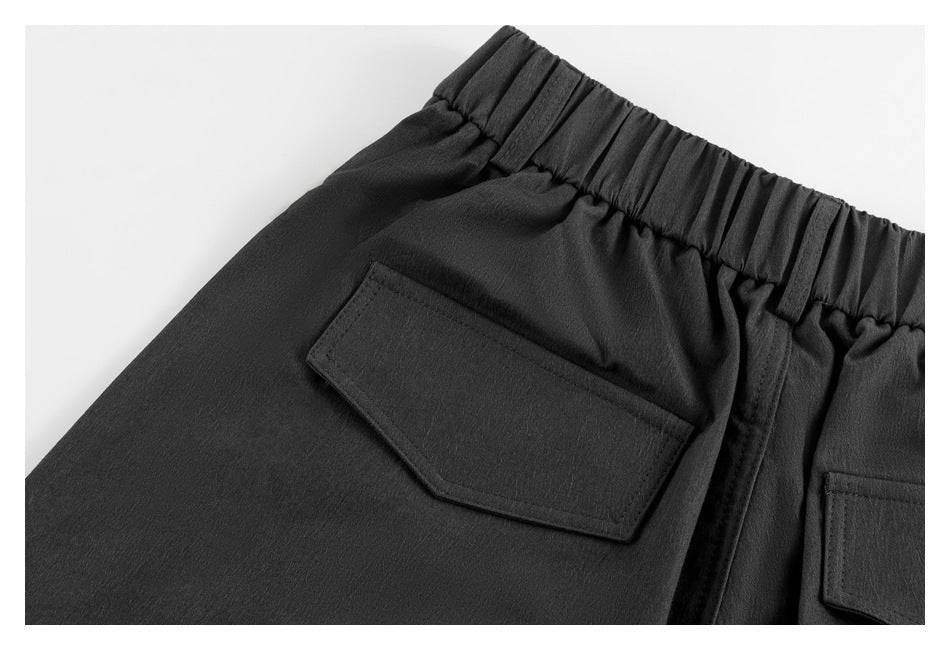 Close-up of black trousers showing a rear flap pocket and gathered elastic waistband.