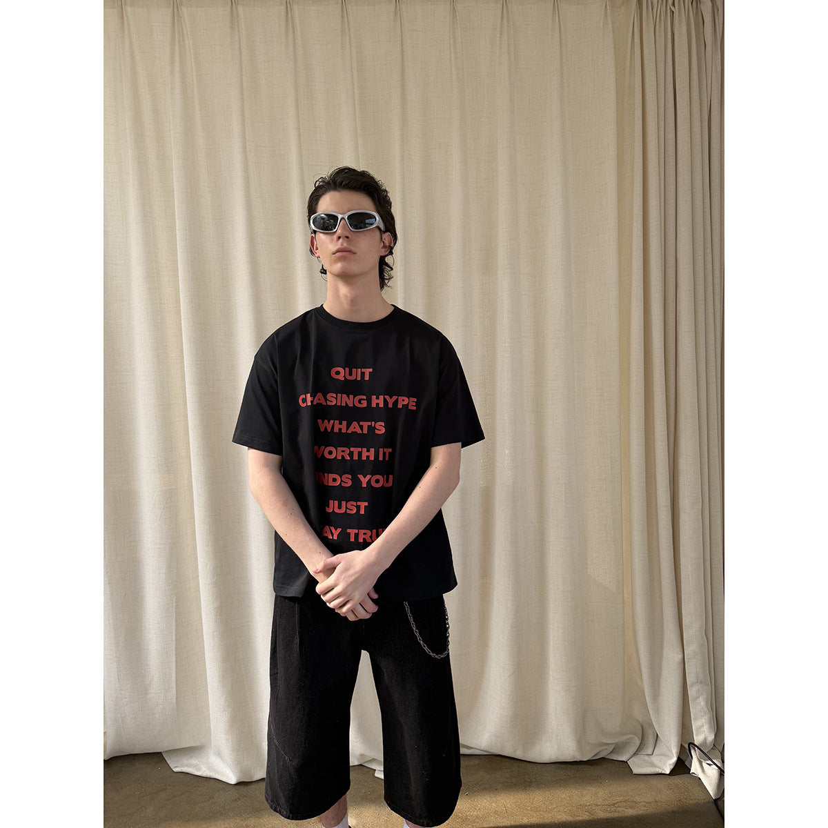 Model wearing a black T-shirt with red lettering on the front, black shorts and sunglasses.
