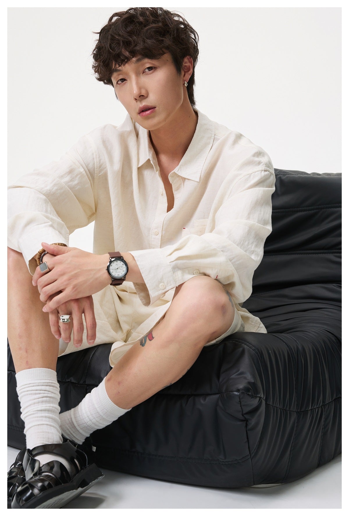 Man seated on a black cushioned seat wearing beige shorts with a matching long-sleeve shirt, white socks and black sandals