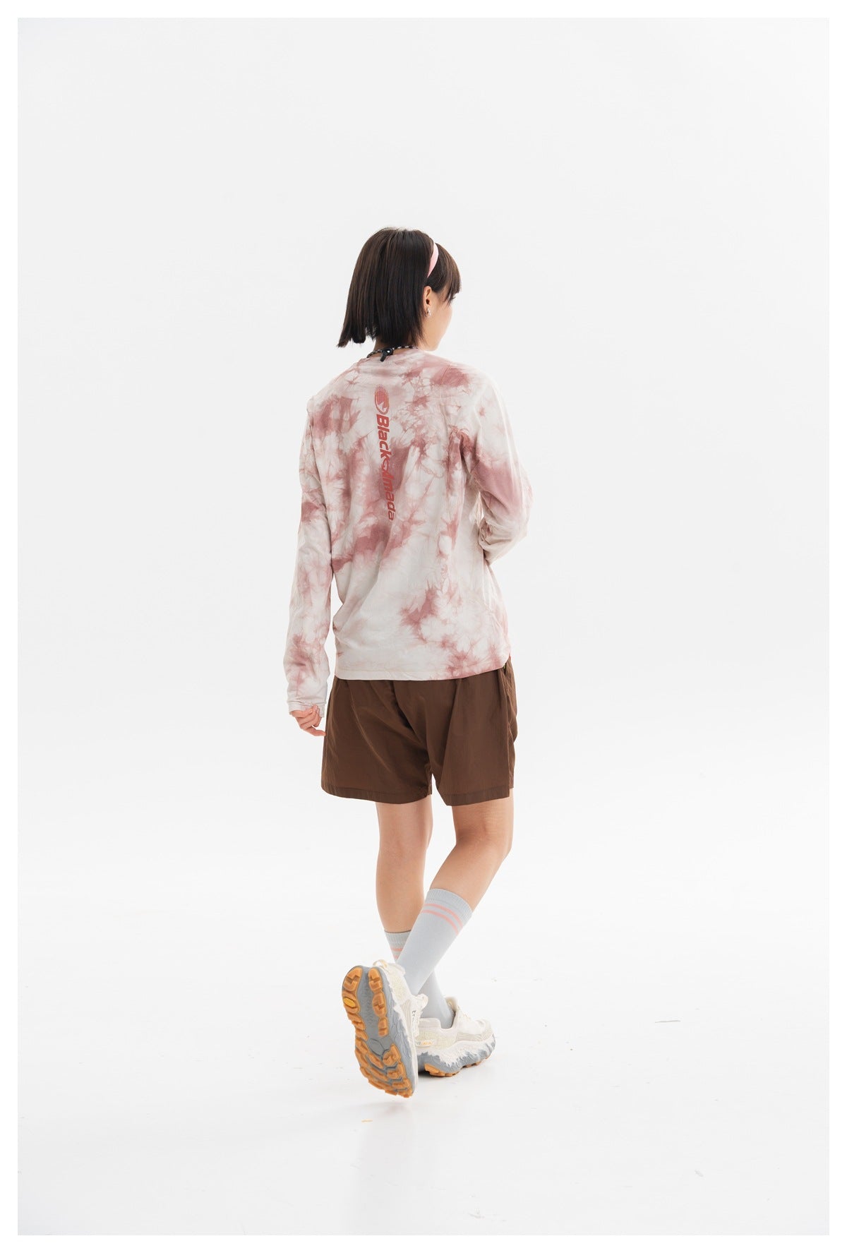 Model shown from behind wearing a cream and dusty-pink tie-dye long-sleeve shirt with brown shorts.