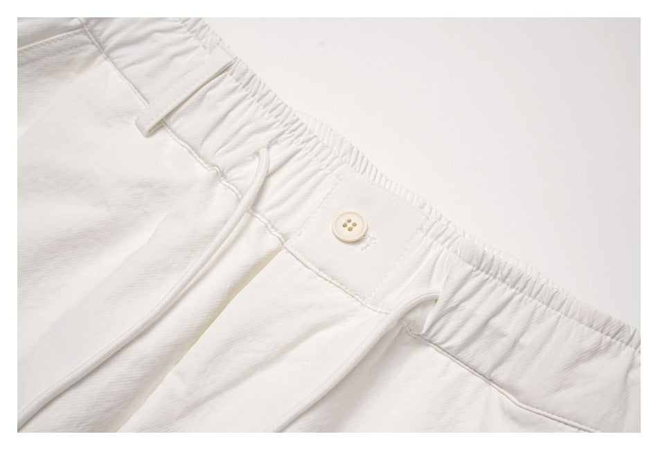 Close-up of the off-white trousers' gathered waistband, button closure and drawcord.