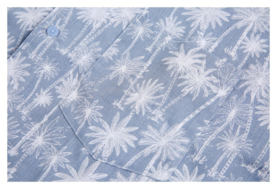 Close-up of a light blue garment with white palm-tree print, a button, and a patch pocket.