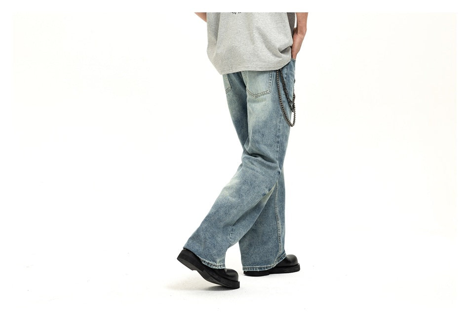 Rear three-quarter view of a model wearing loose light-wash blue jeans with back pockets and a hanging chain.
