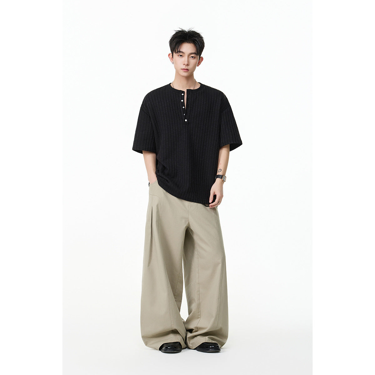 Model wearing a black ribbed short-sleeve henley with beige wide-leg trousers.