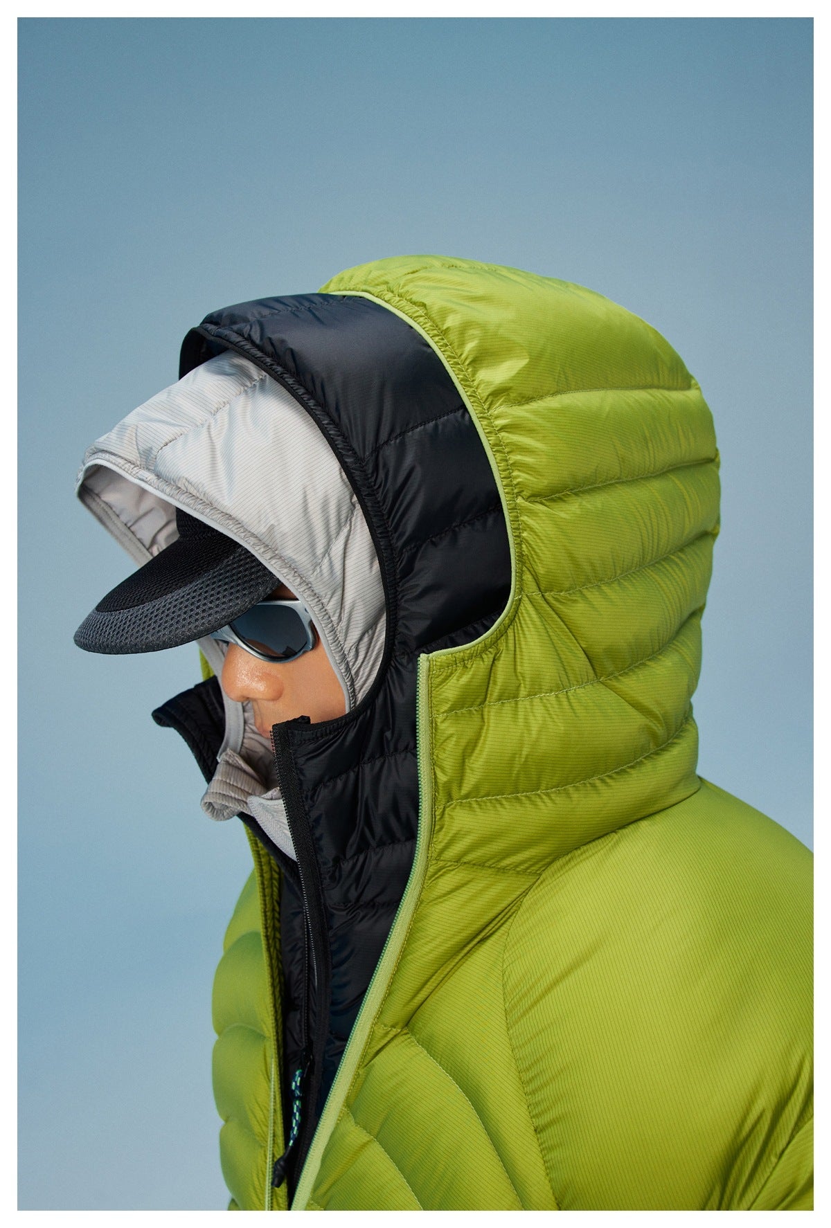 Close-up of a model wearing a lime-green quilted jacket with a raised hood, black trim, and layered inner hood.