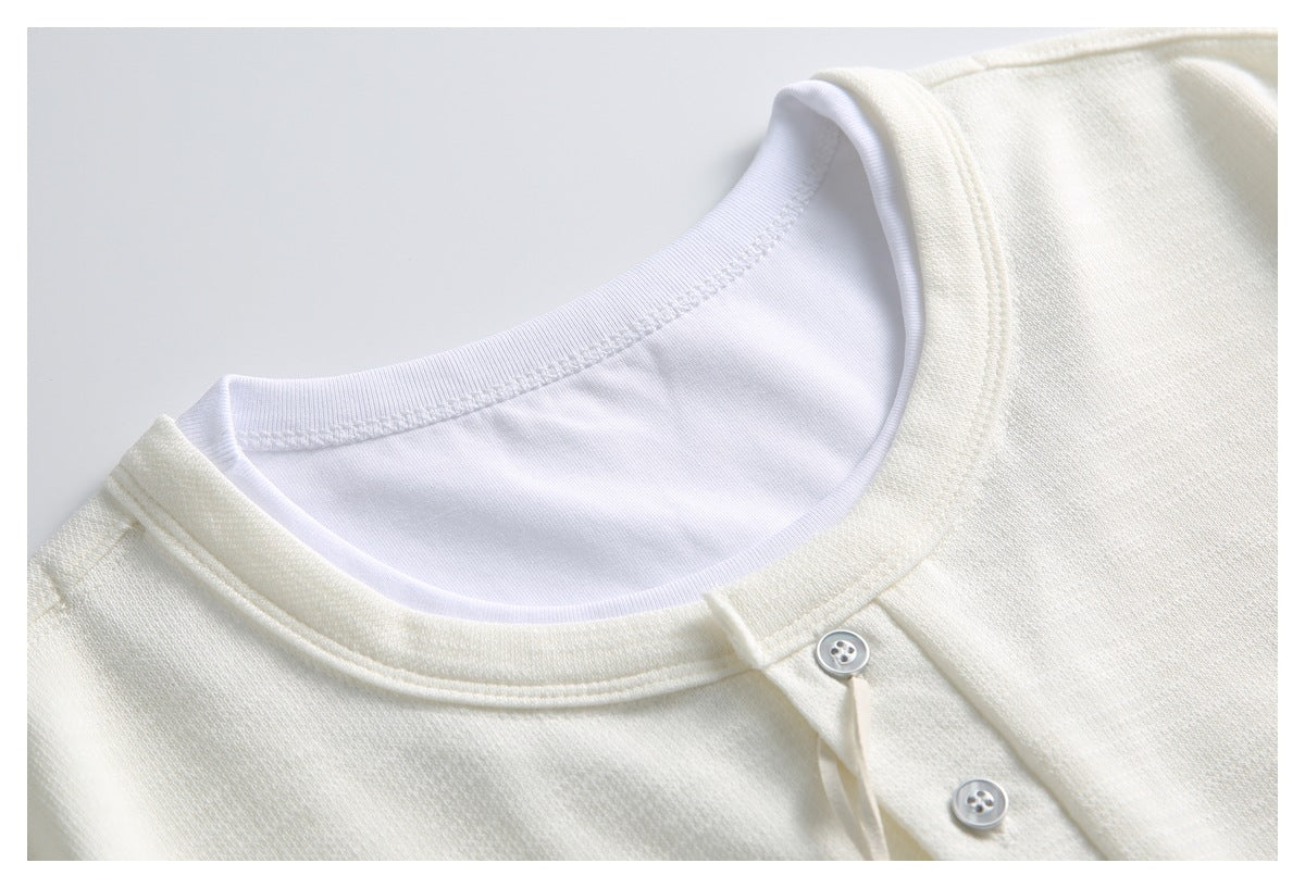 Close-up of an ivory knit top's rounded neckline, white inner layer and two-button front placket.