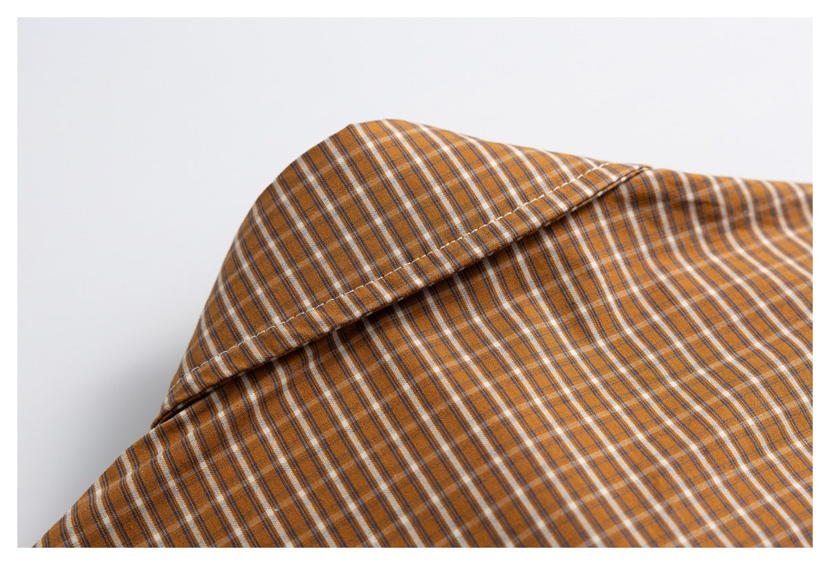 Close-up of a curved stitched seam across the shoulder area of the brown plaid shirt.