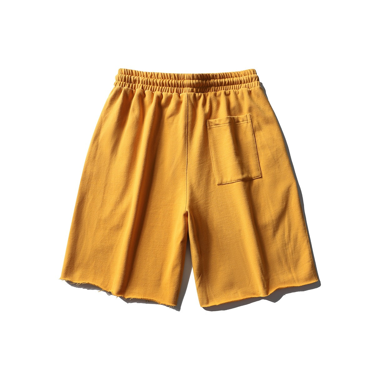 Back view of mustard-yellow shorts with an elastic waistband, a single patch pocket, and raw hems.