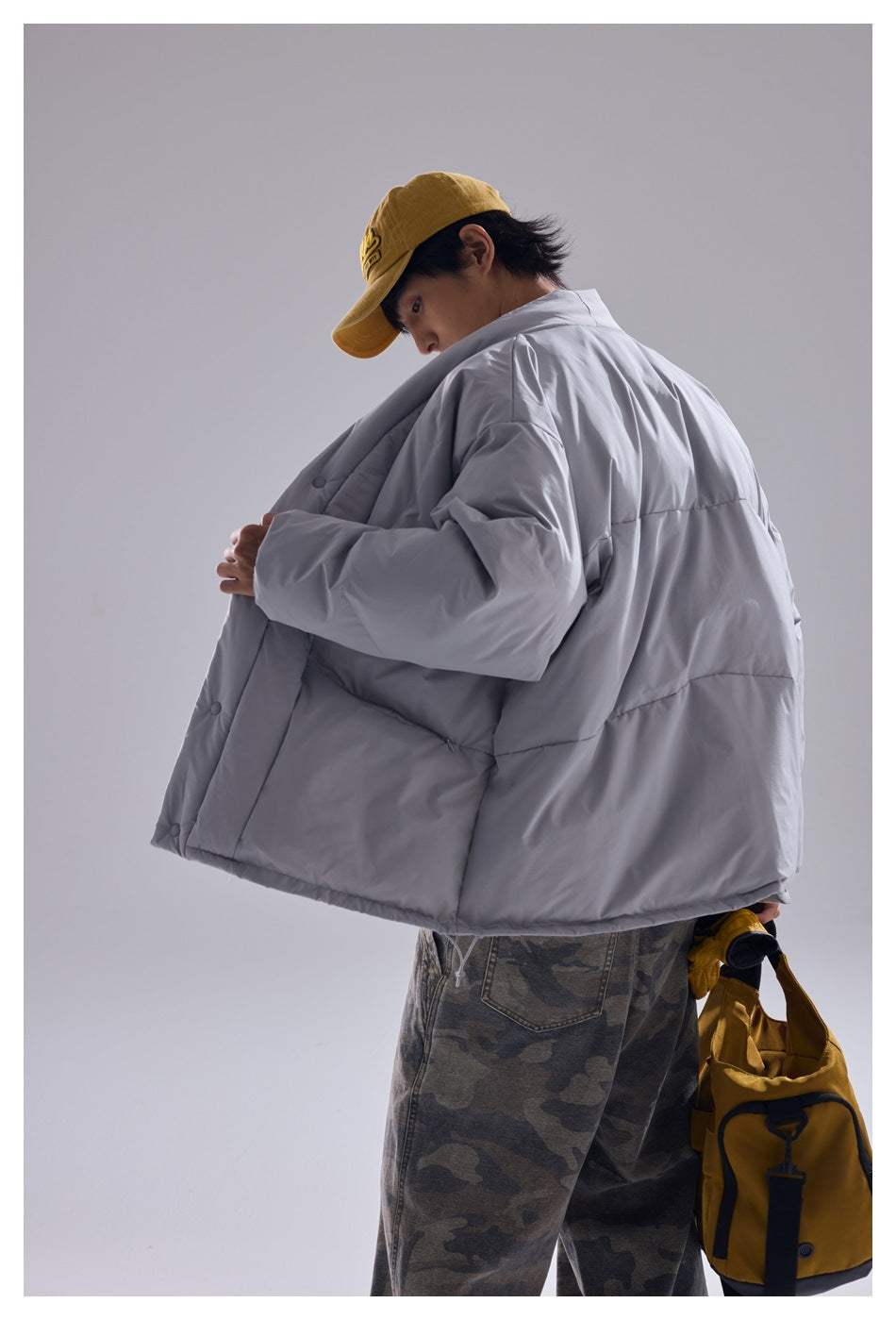Rear view of a model wearing an oversized light gray quilted jacket with a wide back panel and snap front.