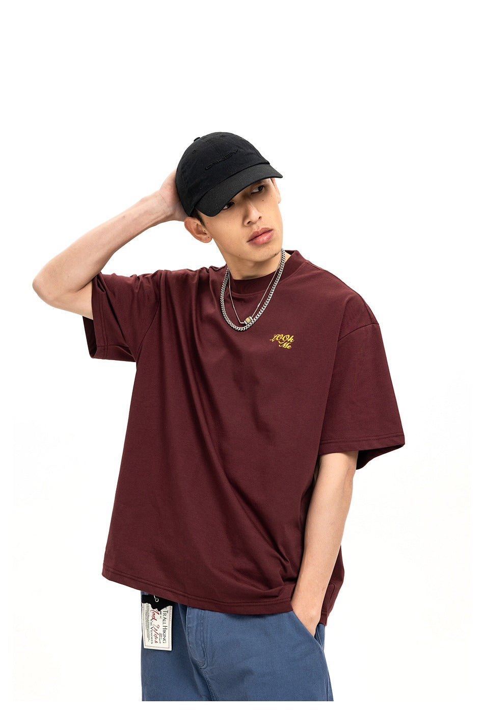 Model wearing a burgundy oversized T-shirt with small yellow chest script, shown from the front.