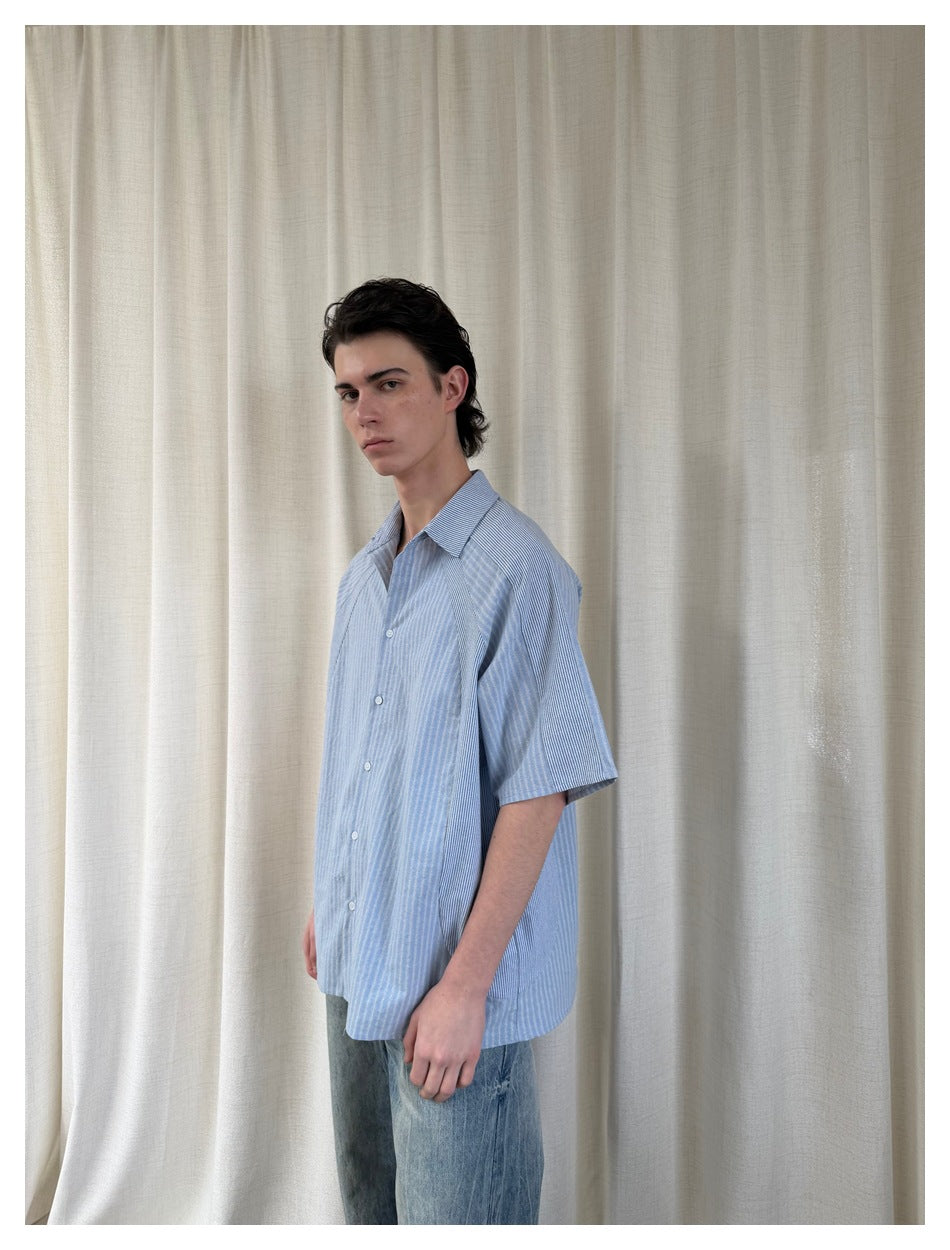 Closer angled view of a model in a light blue striped short-sleeve button-up shirt and blue jeans.