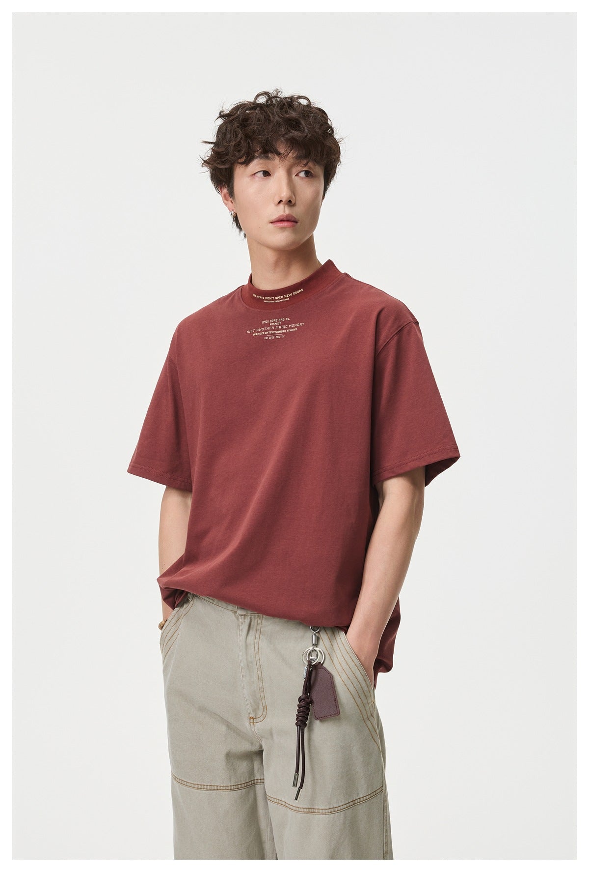 Model wearing a burgundy short-sleeve T-shirt with small cream text at the chest and high neckline.