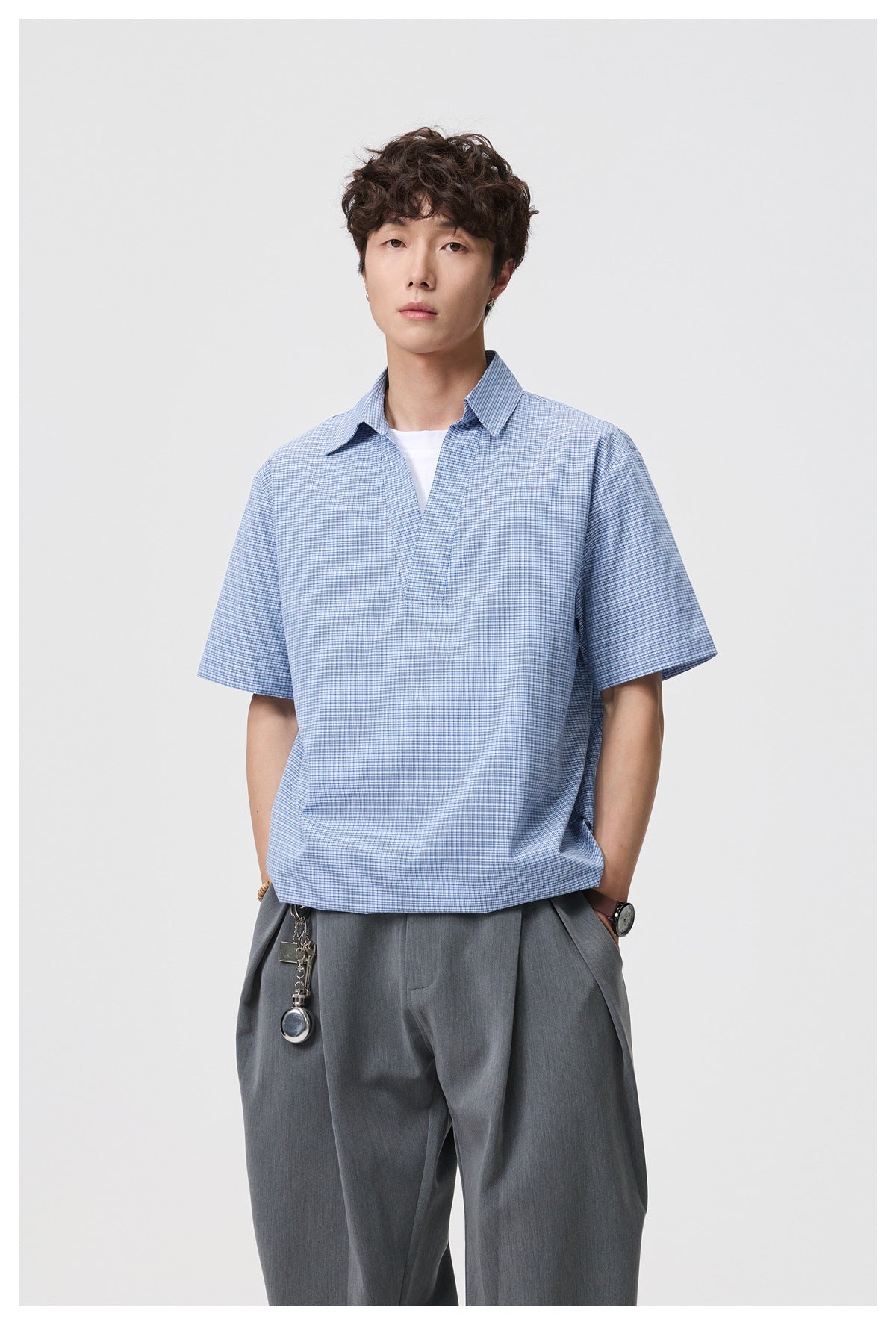 Model wearing blue check short-sleeve V-neck collared shirt over a white top with gray trousers, front view