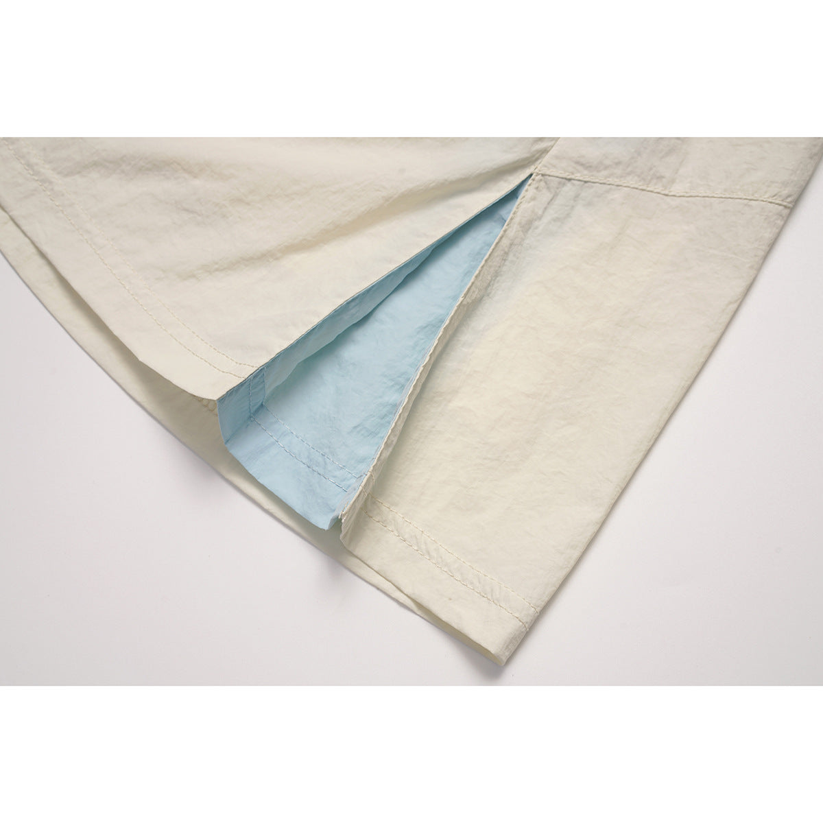 Close-up of an ivory skirt's side slit, showing a pale blue inner panel and stitched hem.
