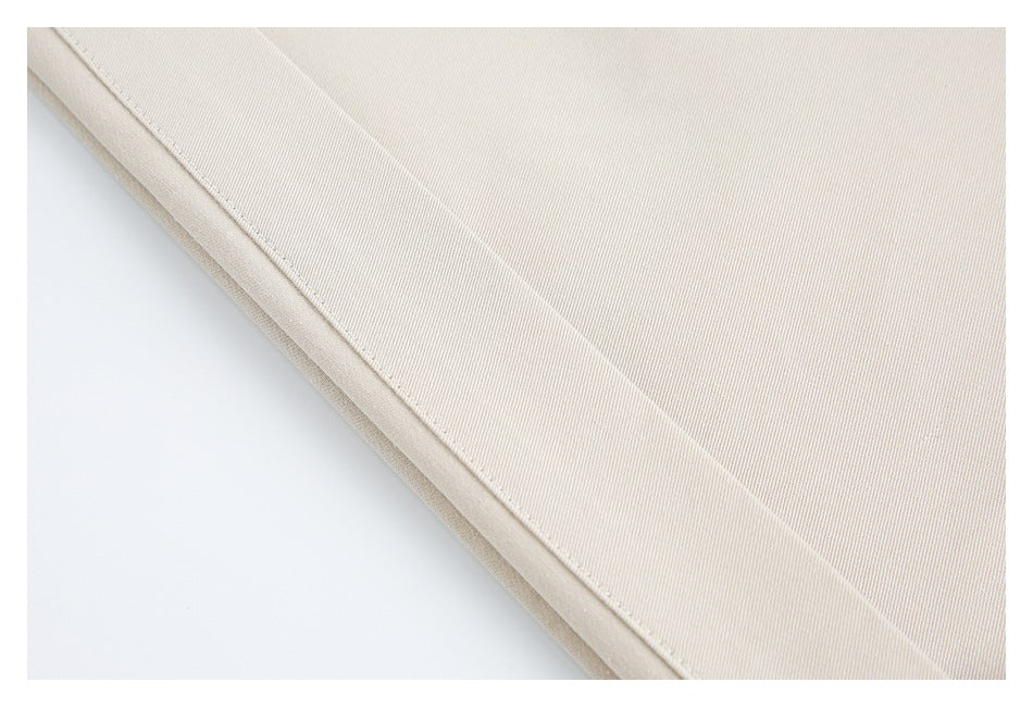 Close-up of light beige garment fabric with a neatly stitched folded edge.