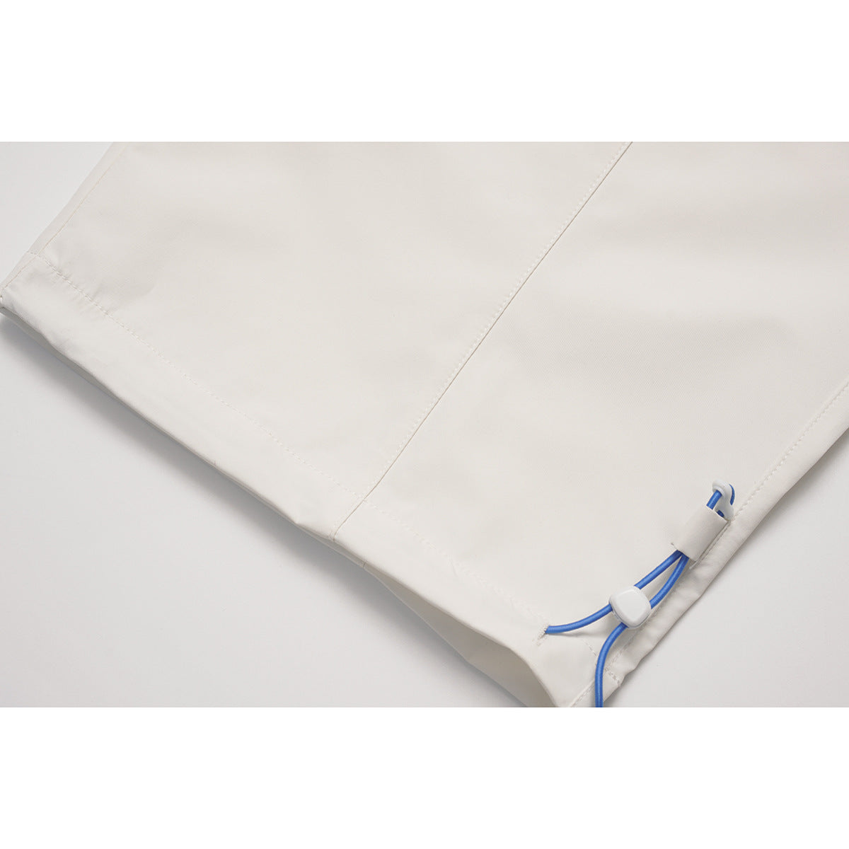 Close-up of a white pants leg hem with a blue adjustable drawcord and cord lock.
