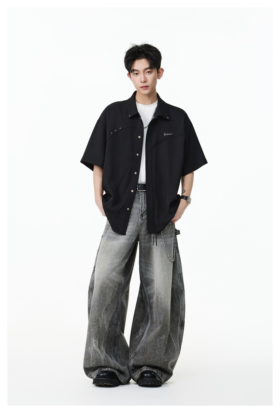 Full-length view of a model wearing a black short-sleeve button-up shirt and oversized gray jeans.