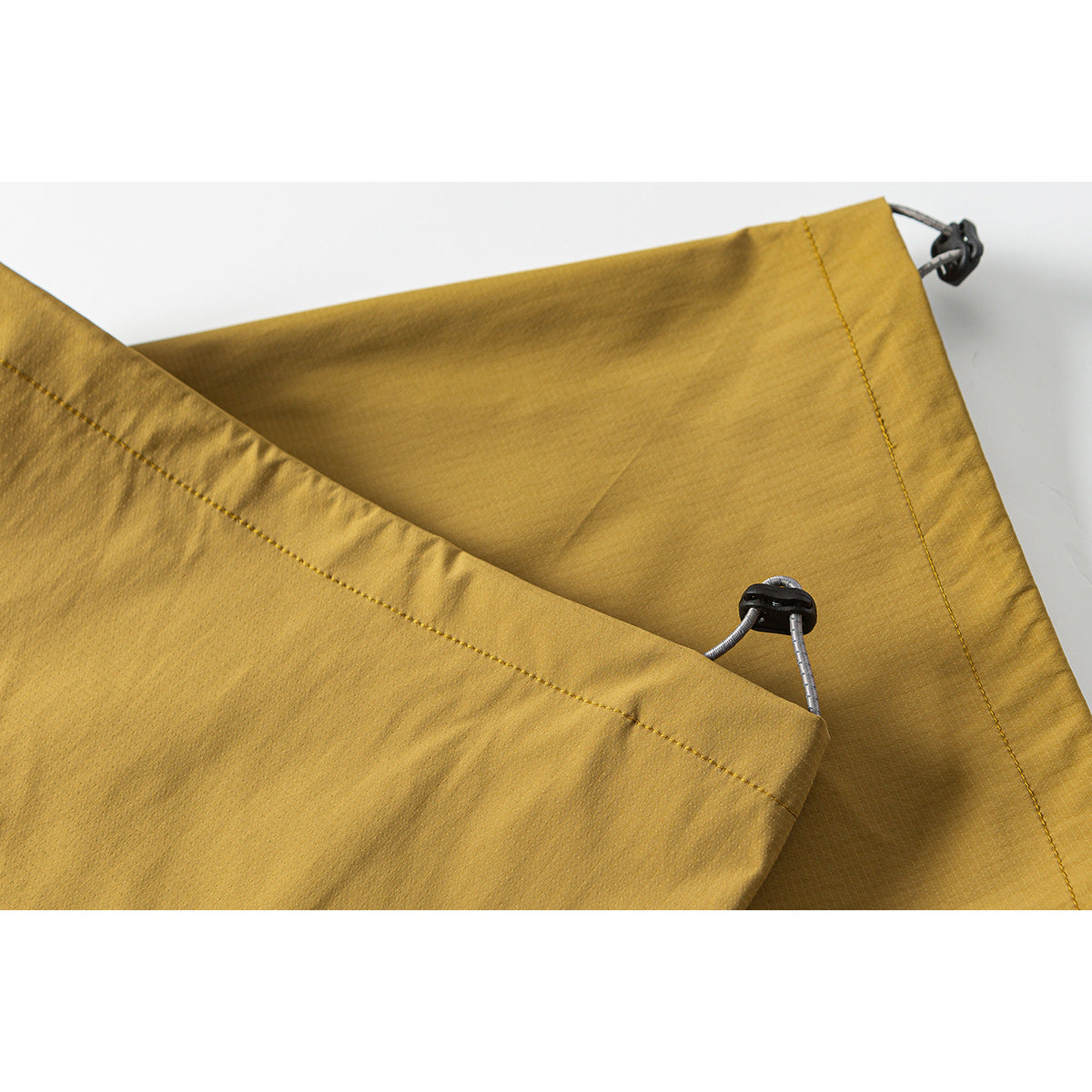 Close-up of mustard-yellow trouser hems with cord-and-toggle adjustment details.
