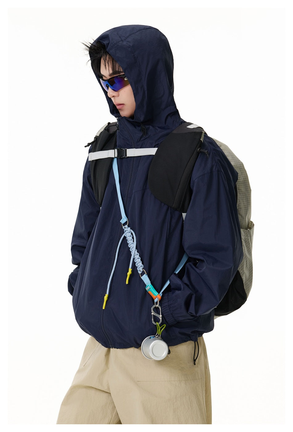 Close view of a model wearing a navy hooded jacket with backpack straps and a clipped accessory.