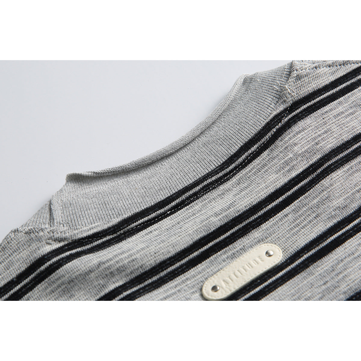 Close-up of the gray ribbed neckline, black stripes, and a small cream-colored tab on the shirt.