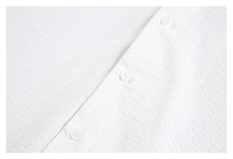 Close-up of a white textured shirt front with three white buttons along the placket.