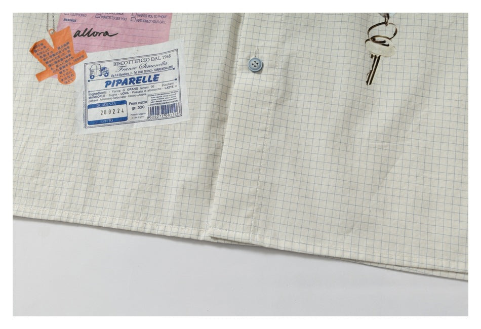 Close-up of the lower front hem of a cream, blue-grid shirt with graphic patches and a key motif.
