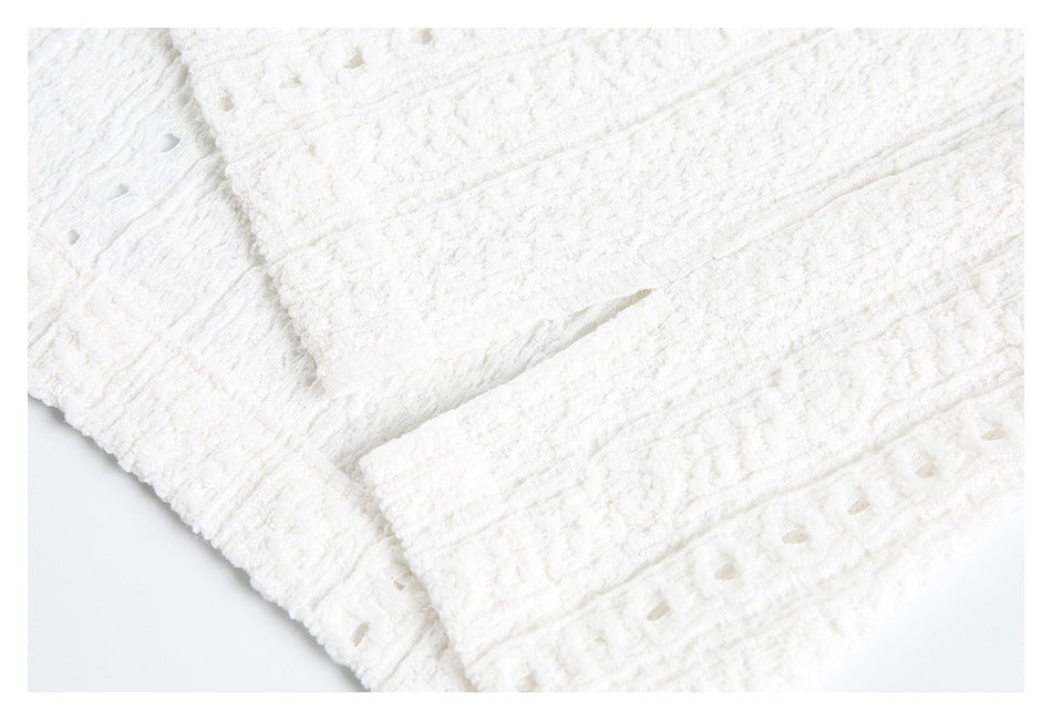 Close-up of white textured garment showing a seam opening and eyelet trim along the edge.