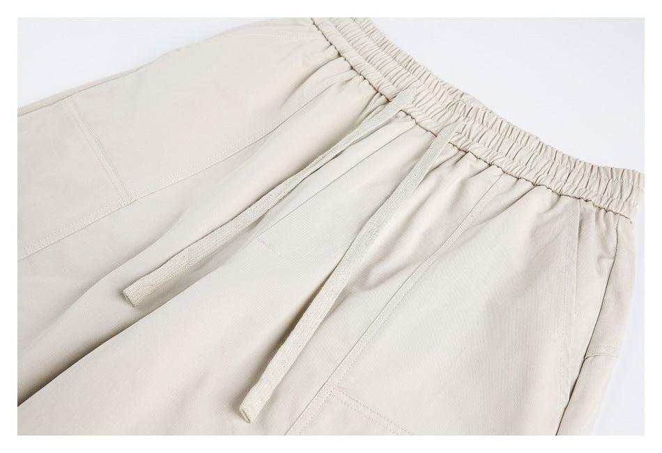 Close-up of light beige pants showing an elastic waistband, two drawstrings, and stitched seams.