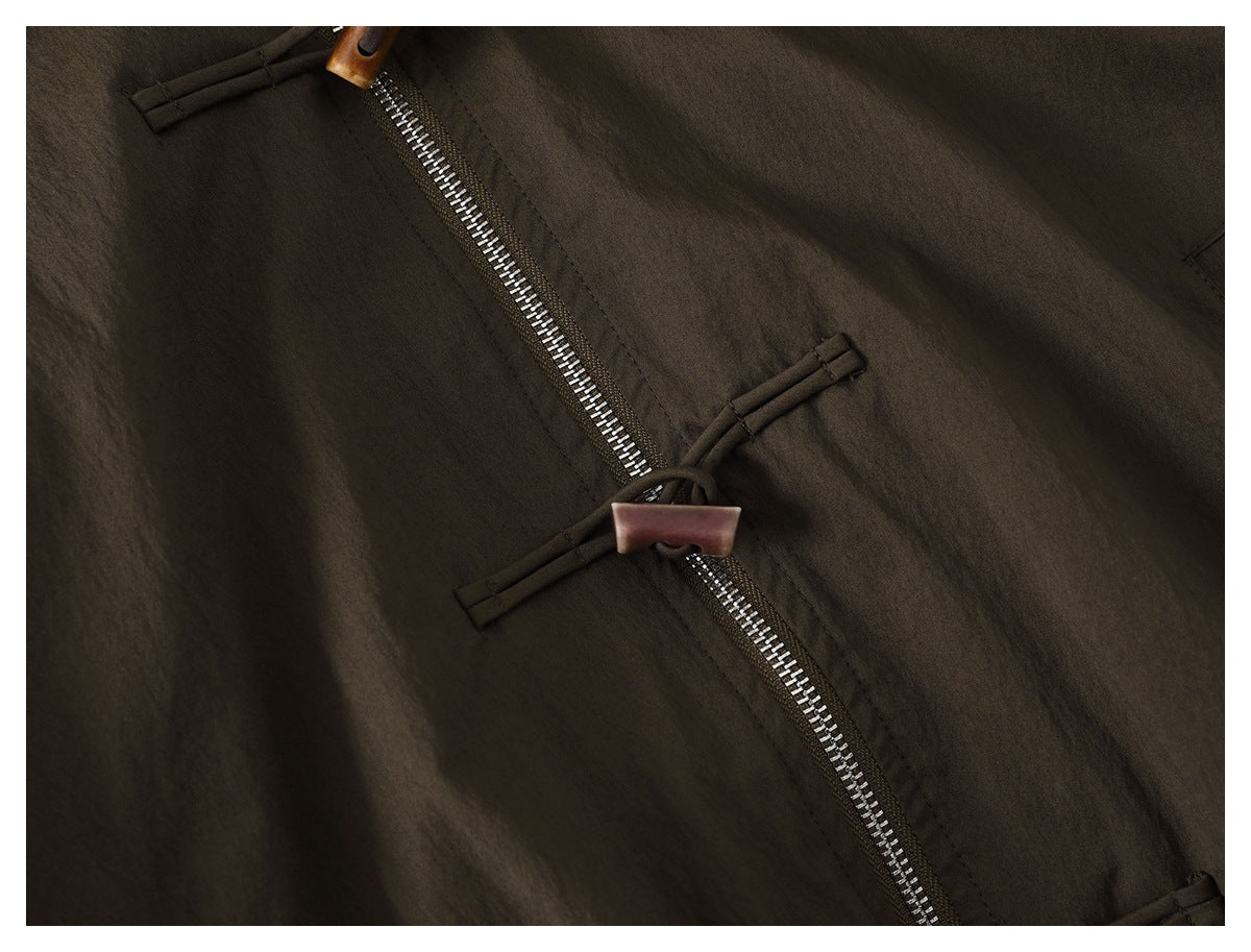 Close-up of the jacket’s diagonal metal zipper and toggle fastening on dark olive-brown fabric.