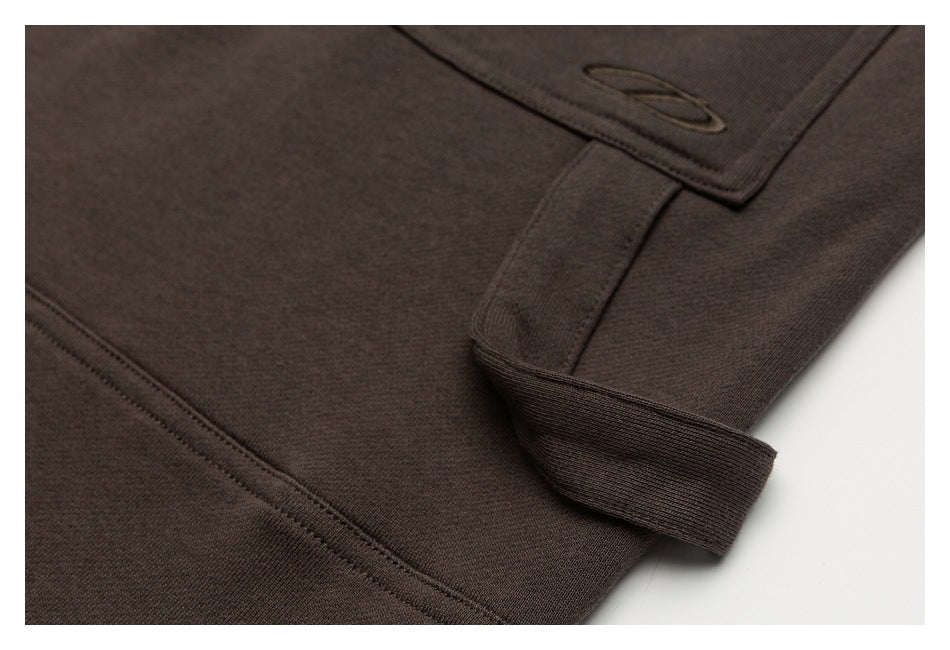 Close-up of dark brown garment construction, showing a ribbed cuff and part of a stitched pocket.