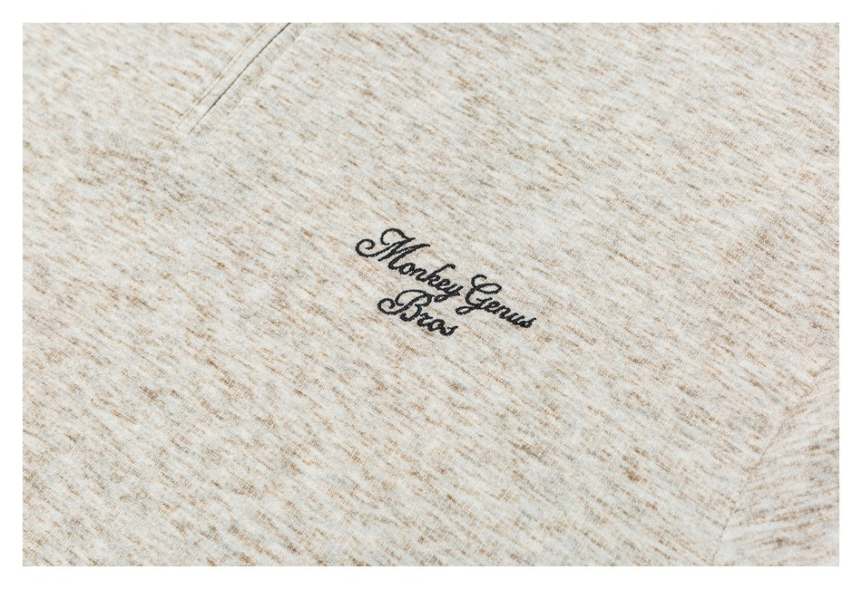 Close-up of black cursive “Monkey Genius Bros” embroidery on beige marled fabric.