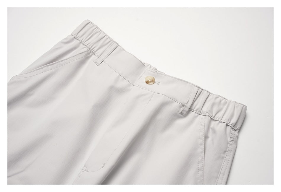 Close-up of off-white pants showing the button closure, belt loops and gathered elastic waistband.