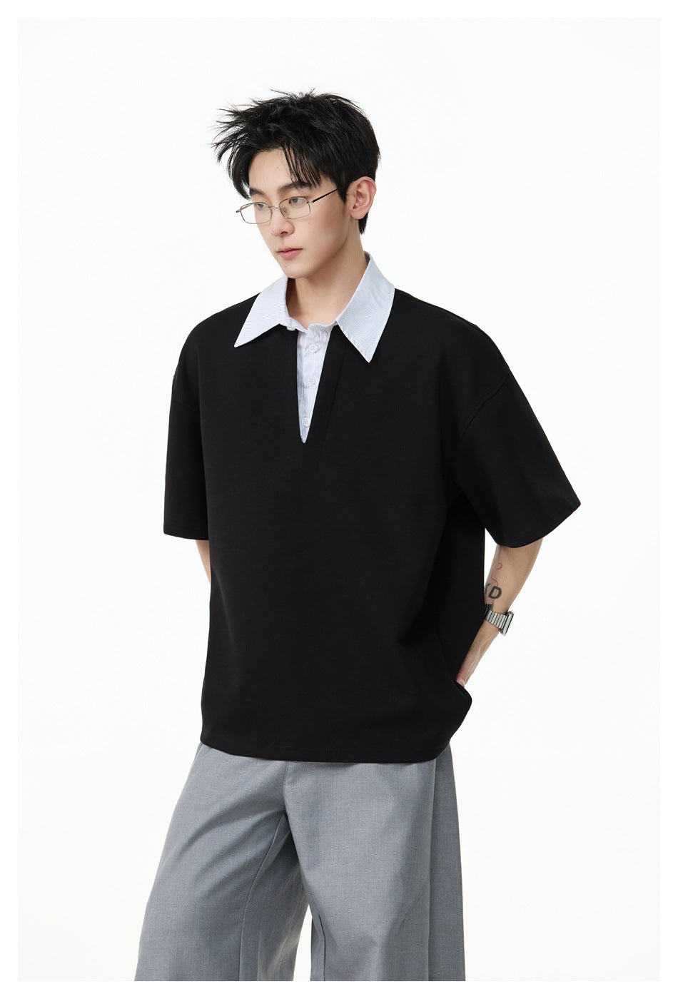 Model in a black short-sleeve top with a pinstriped collar and V placket, shown at three-quarter length with gray trousers