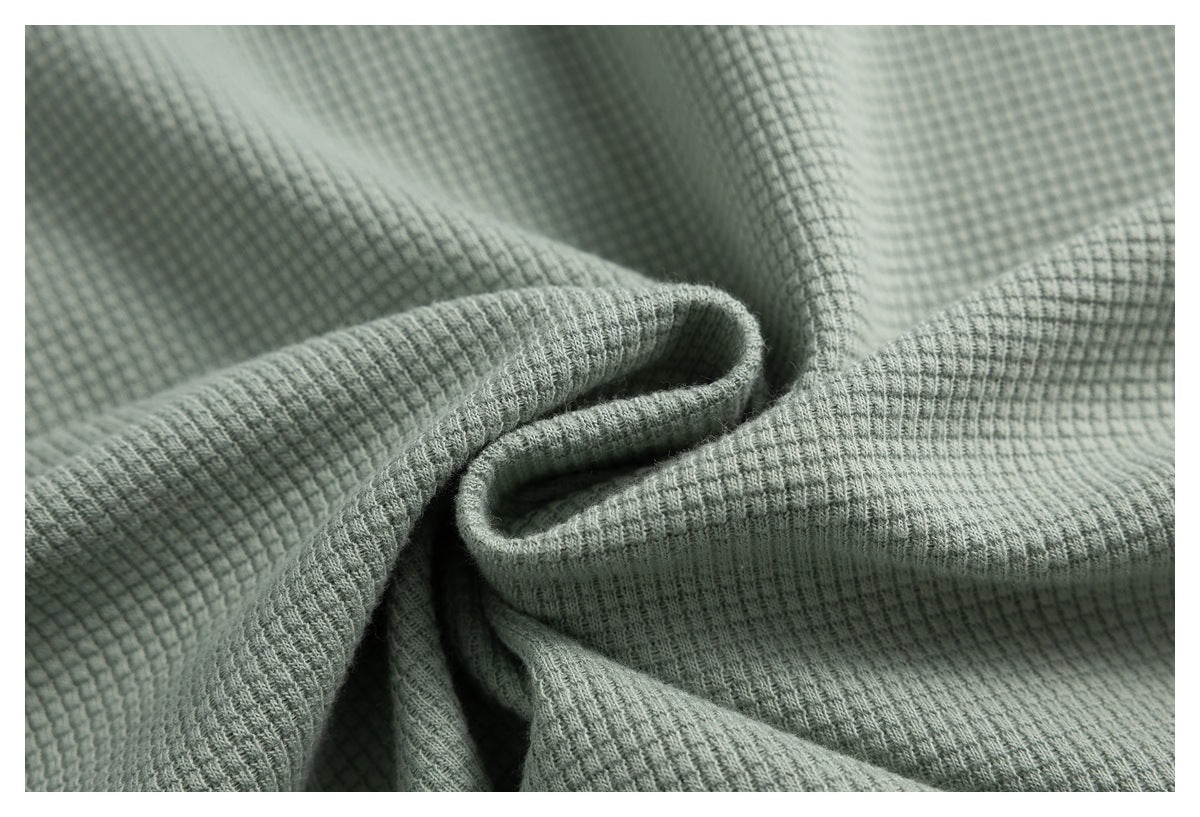 Close-up of sage green fabric showing a raised grid texture and soft folds.