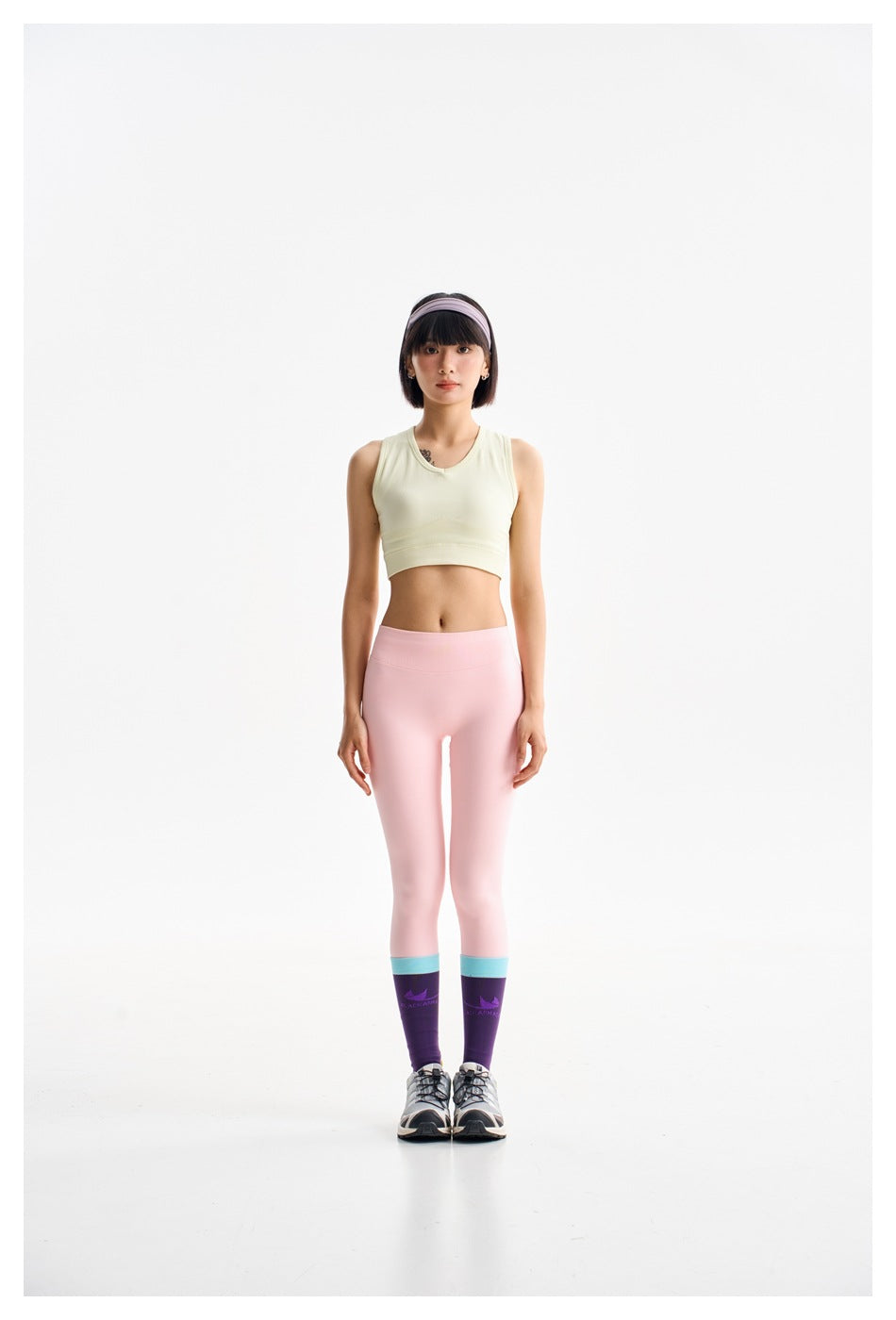 Front view of a model wearing a pale yellow cropped tank top and light pink leggings.
