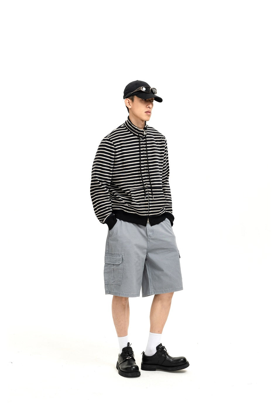 Three-quarter front view of a person wearing a black-and-cream striped zip jacket and light gray cargo shorts.