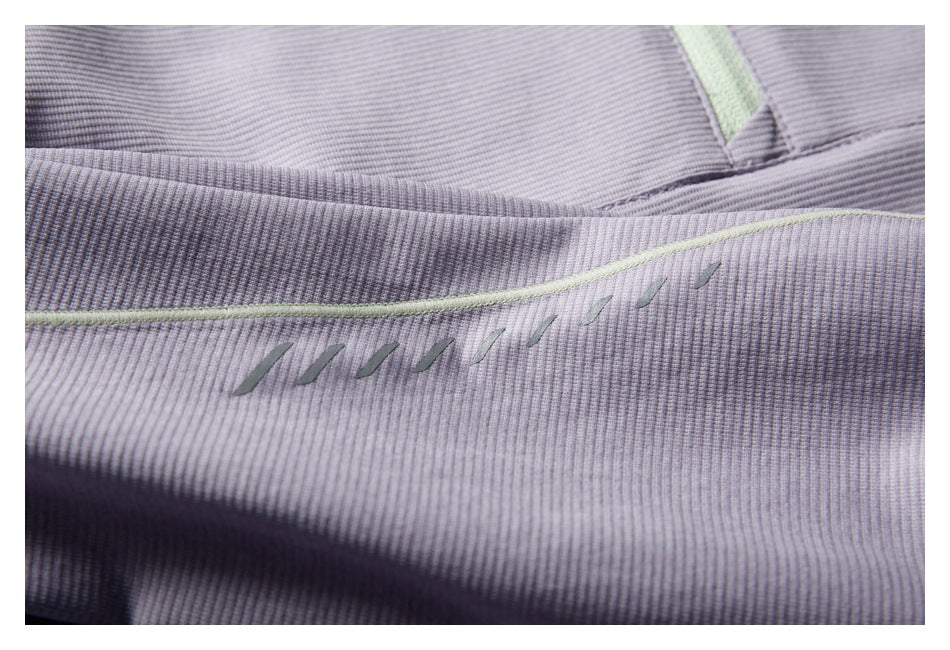 Close-up of a row of small diagonal embroidered marks below pale green piping on the lavender jacket.