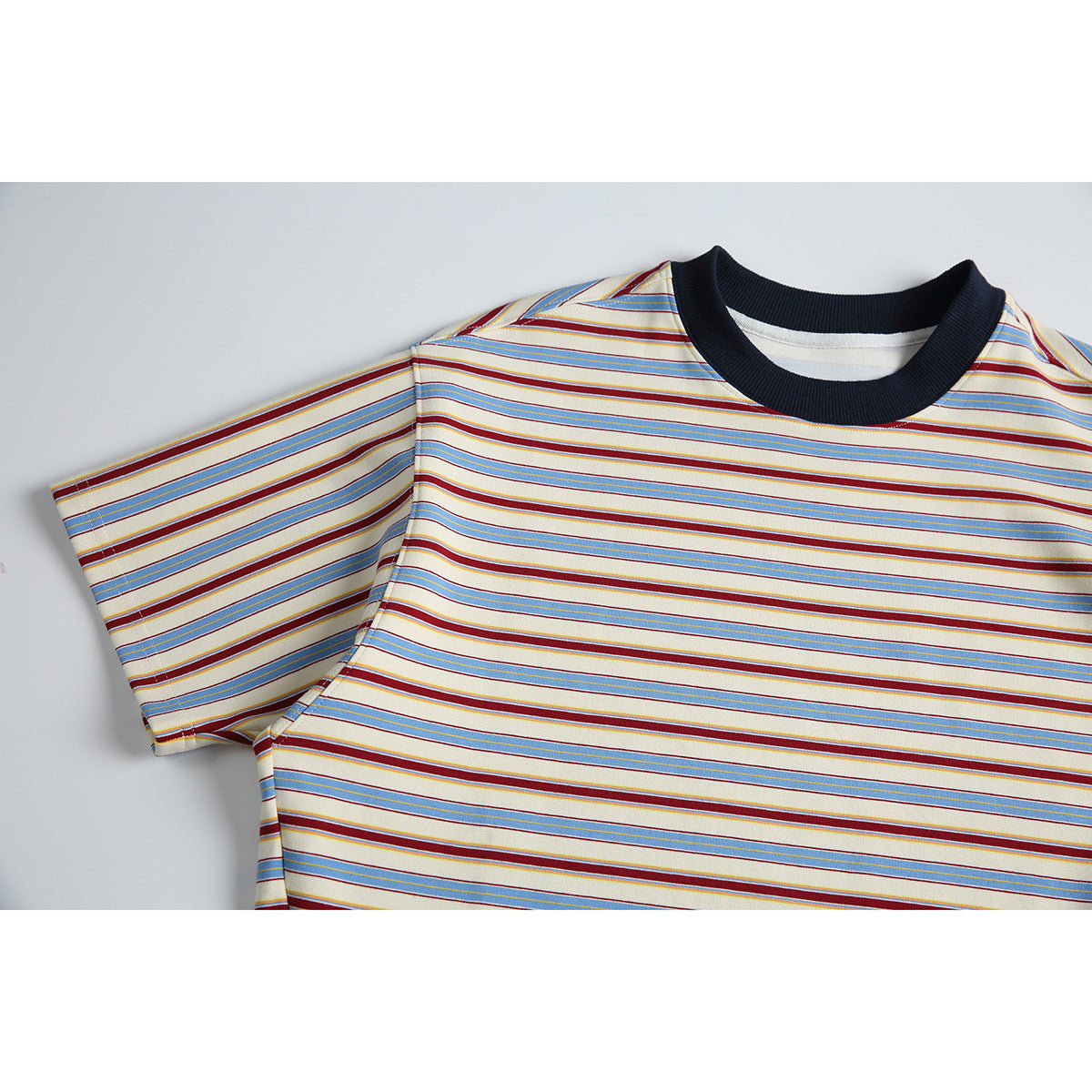 Close-up of a cream short-sleeve T-shirt with blue and burgundy horizontal stripes and a dark ribbed crew neck.
