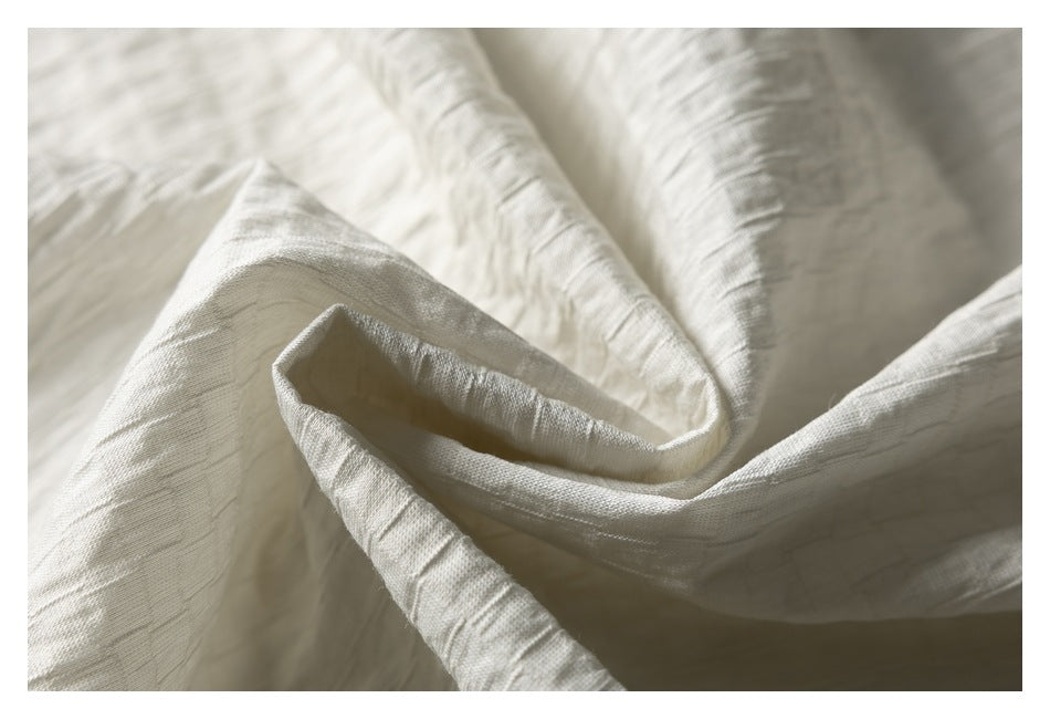 Close-up of softly draped ivory fabric with a visible slubbed weave and deep folds.