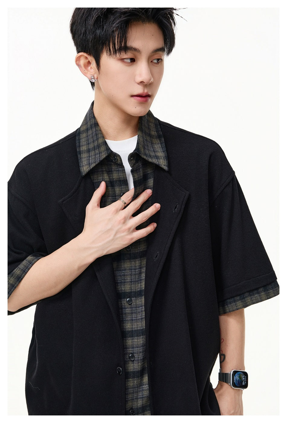 Close-up of model wearing black layered top with plaid shirt visible underneath and plaid collar