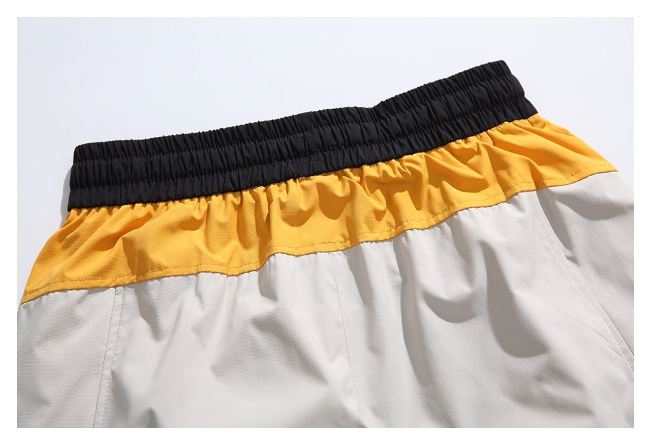 Close-up of light gray shorts with a broad mustard-yellow rear panel and black elastic waistband.