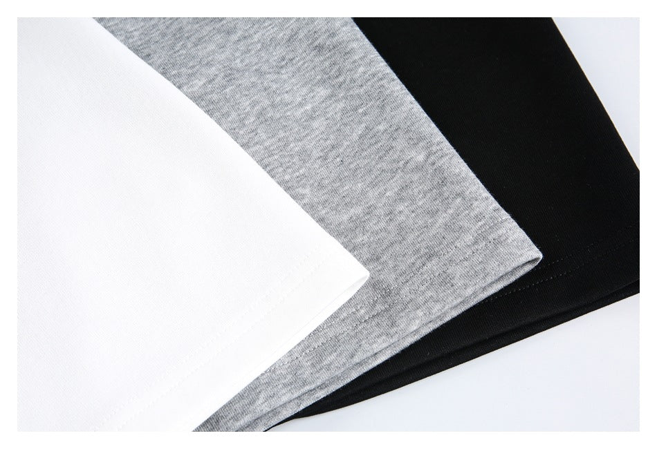 Close-up of the hems and fabric surfaces of white, heather-gray, and black shirts.